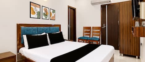 A hotel room with a bed, a desk, a chair, a wardrobe, and a television.
