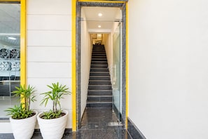 A modern interior with a glass door entrance, a staircase, and potted plants. - Hotel O The Anand Hotel (Zirakpur)
