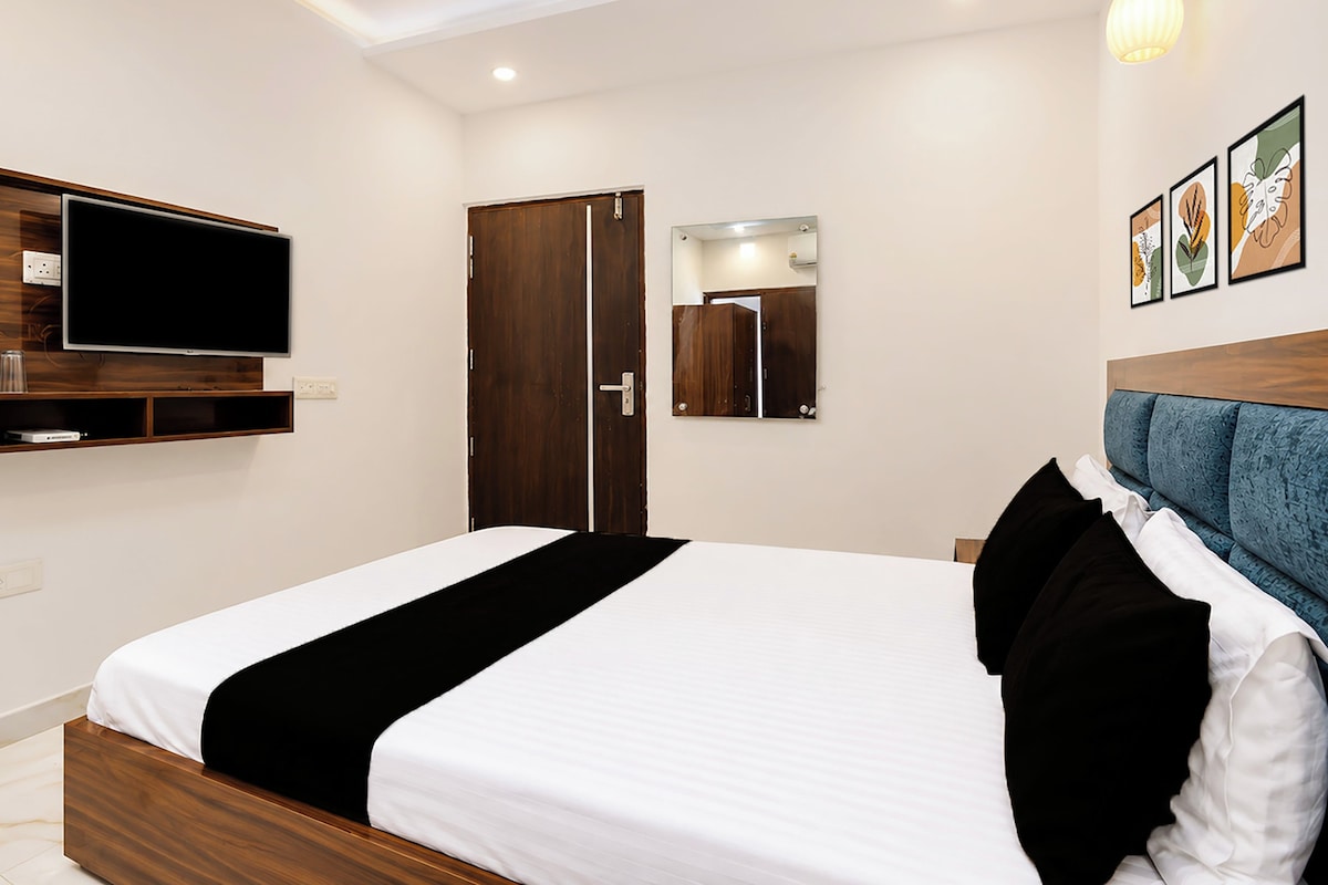 A hotel room with a bed, a television, a wardrobe, and artwork on the wall.