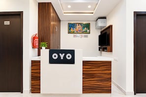 Una recepción con un cartel que dice 'OYO' en un interior moderno con detalles de madera y un televisor montado.