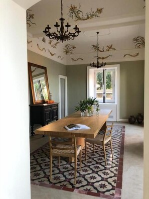 A dining room with a wooden table, chairs, a chandelier, and a patterned rug. - Villa Mabel Boutique Hotel (Taormina)