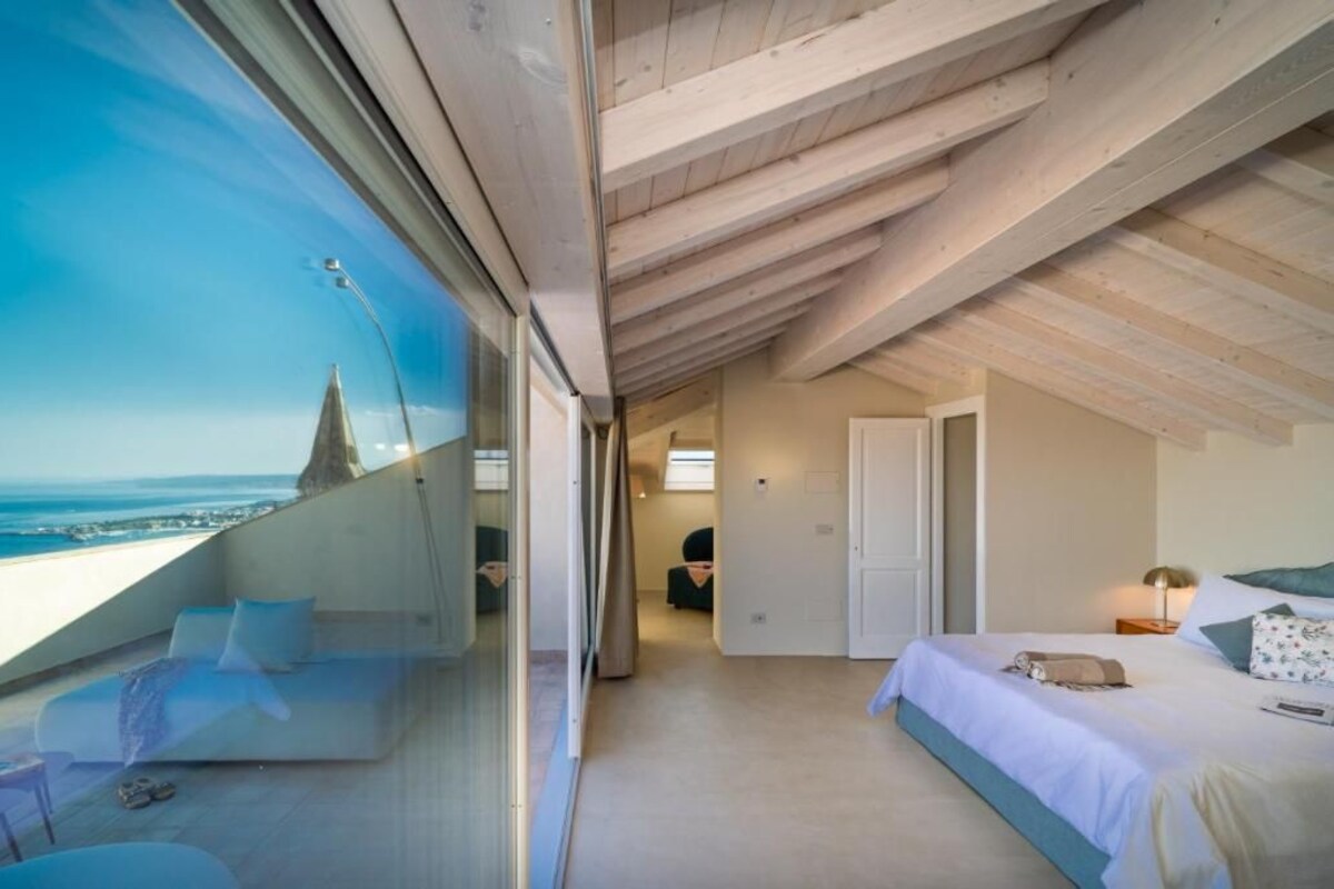 A modern bedroom with a large window overlooking a cityscape, a bed with a nightstand, and a view of the city.