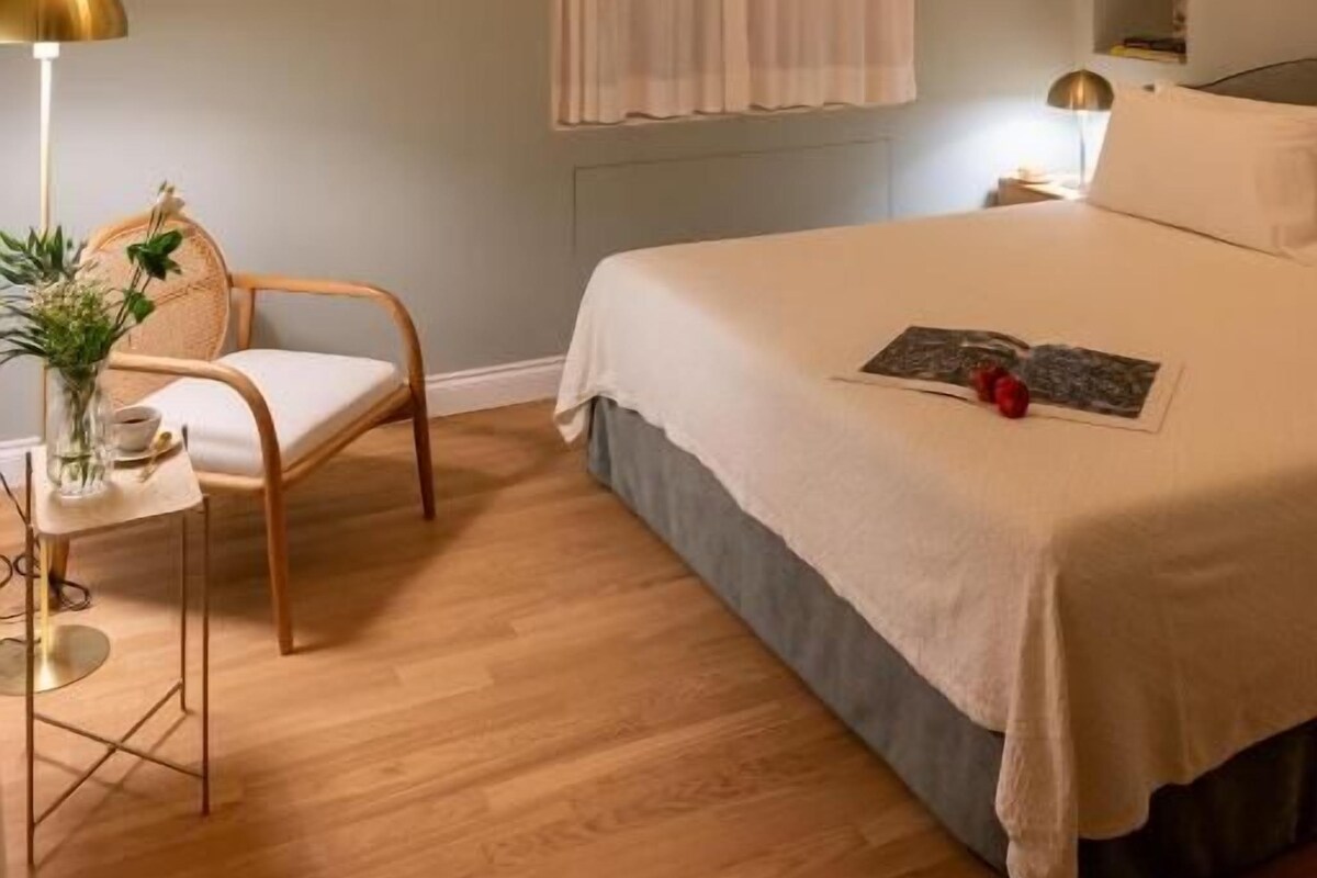 A bedroom with a bed, a chair, a bedside table, a lamp, and a chandelier.