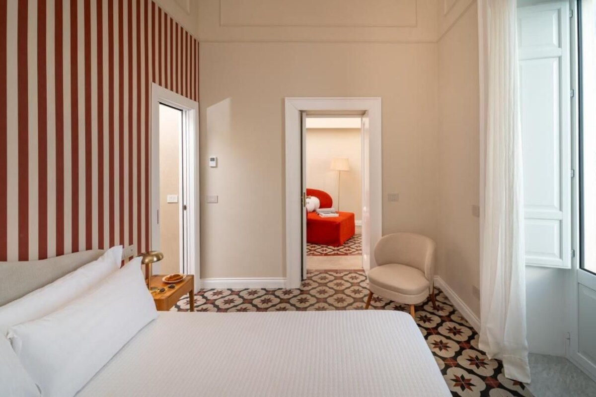 A hotel room with a bed, a chair, a small table, and a door leading to a bathroom.