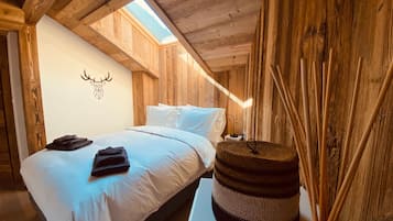 Une pièce en bois avec un lit, une décoration murale représentant une tête de cerf et une lucarne.