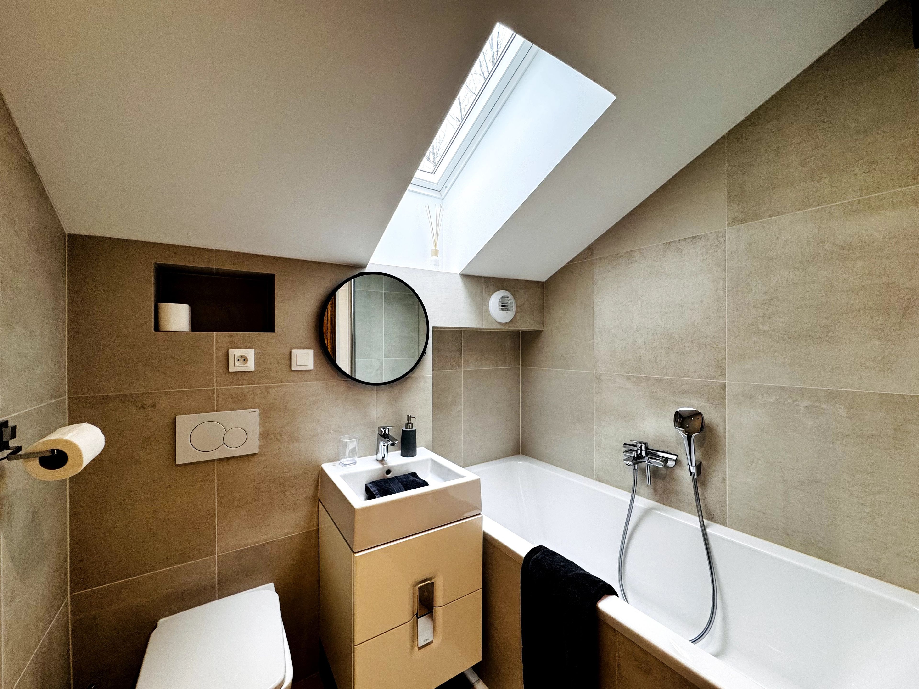 Un baño moderno con tragaluz, inodoro, lavamanos con espejo y bañera.