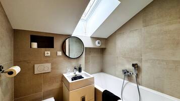 Un baño moderno con tragaluz, inodoro, lavamanos con espejo y bañera.