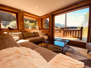 A cozy interior with a sofa, a coffee table, and a view of a deck and mountains. - Chalet with Private Spa and Sauna (Morzine)