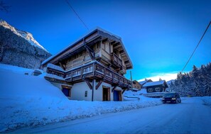 Un chalet en bois à plusieurs étages, doté de balcons, qui se dresse sur fond de montagnes enneigées.