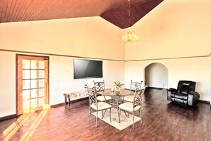 Ein geräumiges Zimmer mit Esstisch, Stühlen, einem Flachbildfernseher, einer Chandelier-Leuchte und einem Ledersofa.