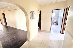 A hallway with a dark carpeted area, a tiled floor, and a door leading to a bathroom with a toilet. - Moorish Mount Cool Breeze Room – Bright Hilltop Double, Mandeville (Mandeville)