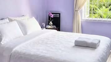 Ein ordentlich bezogenes Bett mit weißen Leinentüchern, ein kleiner Nachttisch mit Blumen in einer Vase und ein Fenster mit Vorhängen.