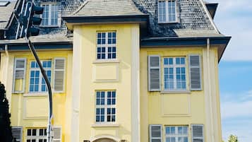 Ein zweistöckiges Gebäude mit einer symmetrischen Fassade, einem zentralen Eingang mit einem Zierbogen und einem Schornstein.