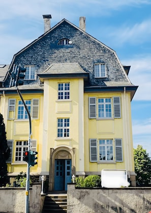 Ein zweistöckiges Gebäude mit einer symmetrischen Fassade, einem zentralen Eingang mit einem Zierbogen und einem Schornstein.