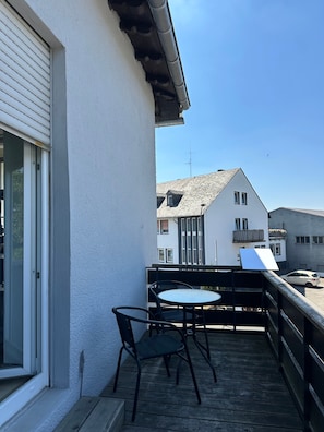 Un balcon avec une table et des chaises, un mur blanc et une vue sur les bâtiments voisins.