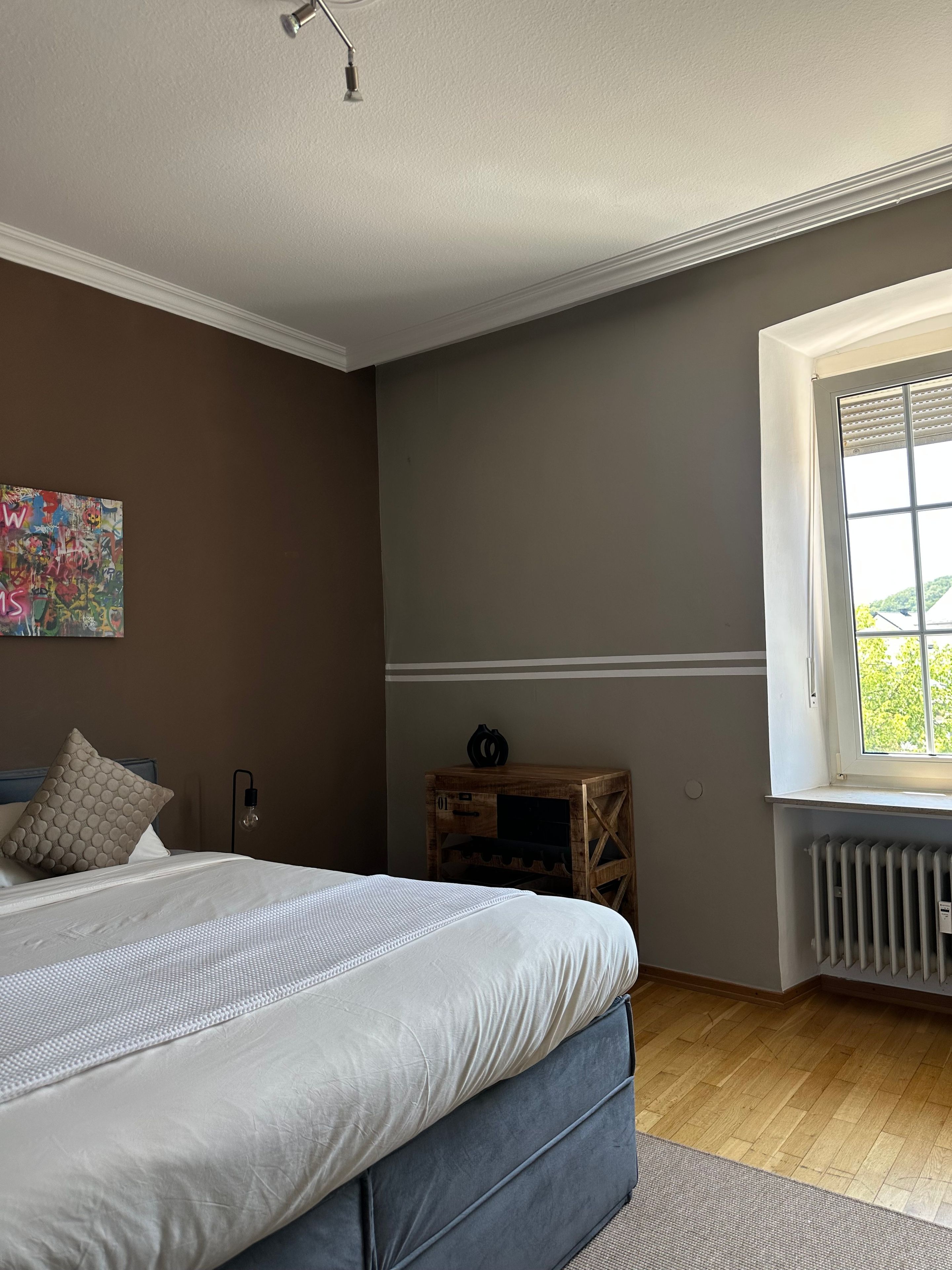 Une chambre à coucher comprenant un lit, une fenêtre, un radiateur et une œuvre d’art accrochée au mur.