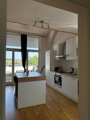 Eine moderne Küche mit weißen Schränken, einer Holzausziehtheke und einem großen Fenster mit Blick ins Freie.