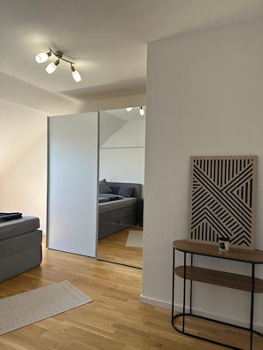 Ein modernes Schlafzimmer mit Schiebetür, einem grauen Sofa, einem Holznachttisch und einem geometrischen Wandbild.