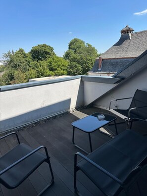 En tagterrasse med et bord og stole, omgivet af en hvid mur og udsigt til træer og bygninger.