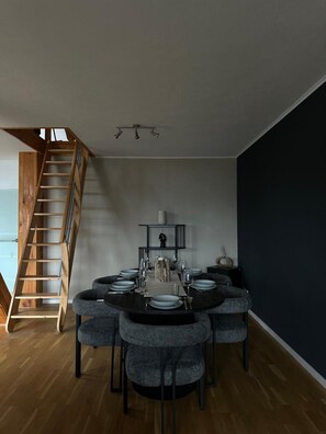 Ein Essbereich mit einem runden Tisch, gedeckt für sechs Personen, einer Holztreppe und einer dunklen Akzentwand.