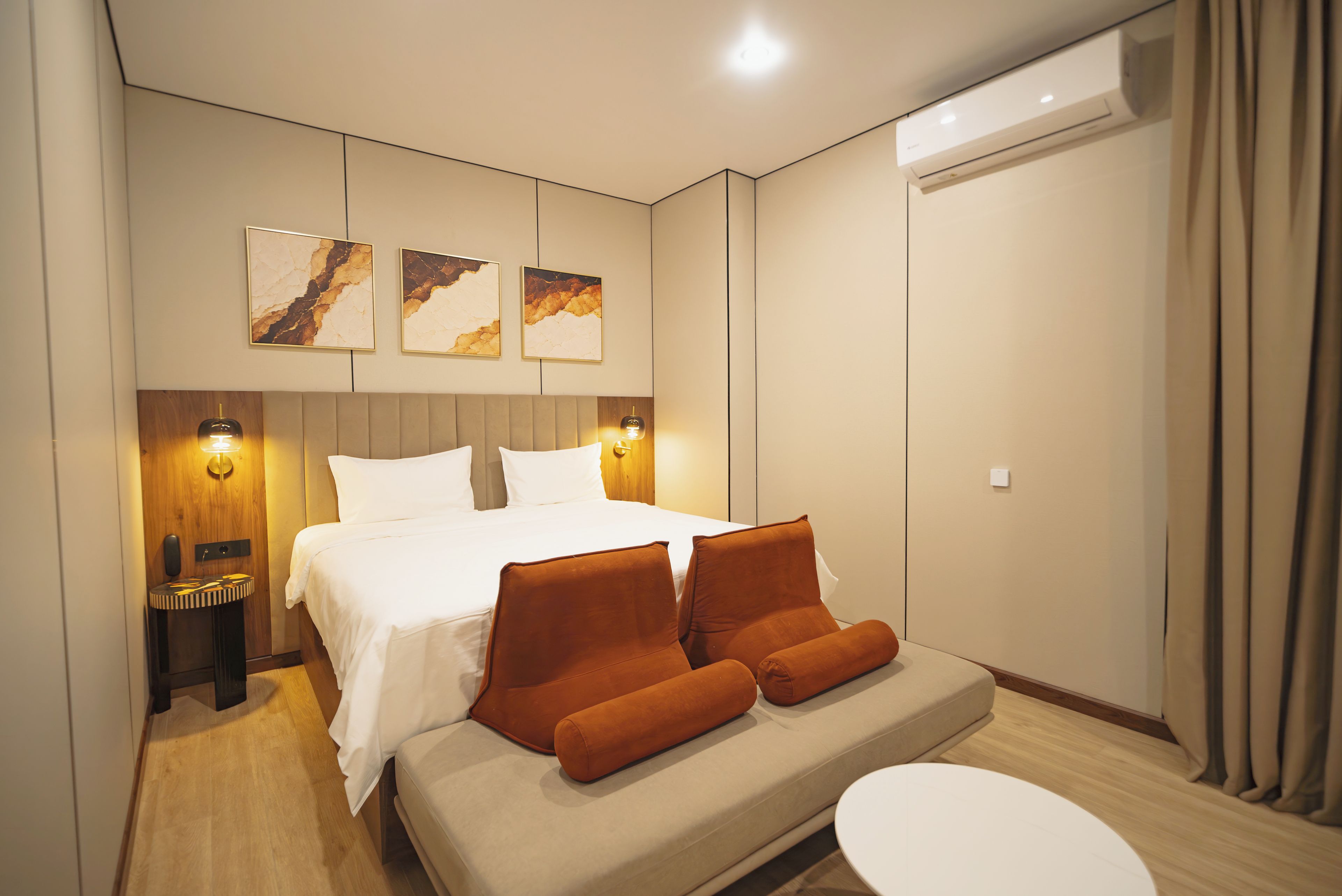 Habitación de hotel moderna con cama, sofá, mesita de noche y aire acondicionado instalado en la pared.