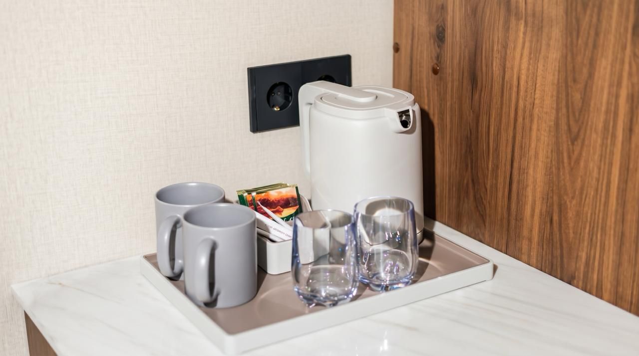 Una bandeja con dos tazas grises, un vaso y una tetera eléctrica blanca sobre una encimera de mármol.