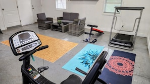 Una palestra in casa con attrezzature per esercizi, un tapis roulant e tappetini da ginnastica.