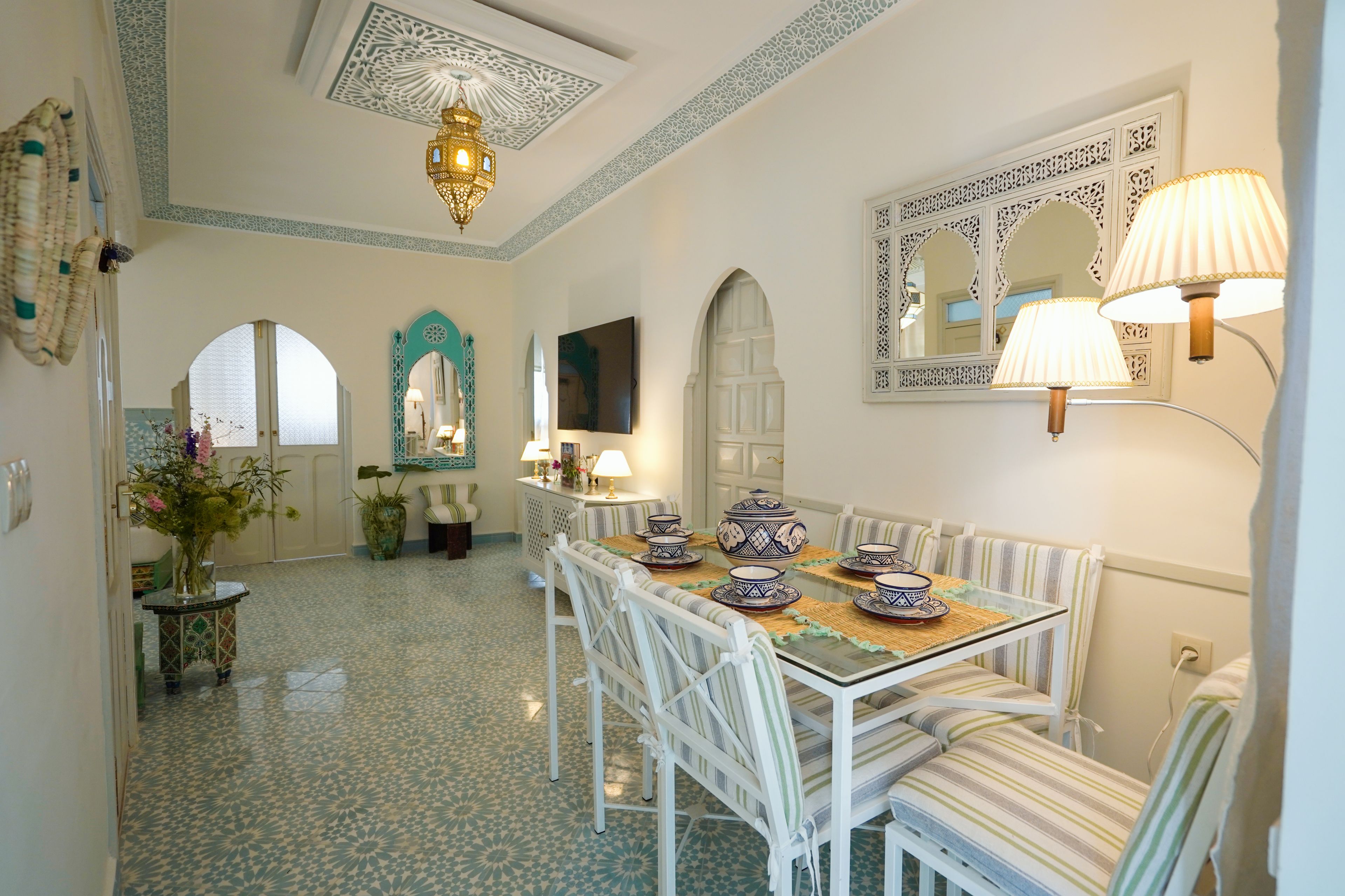 A dining area with a glass table, white chairs, patterned floor tiles, and decorative wall sconces.
