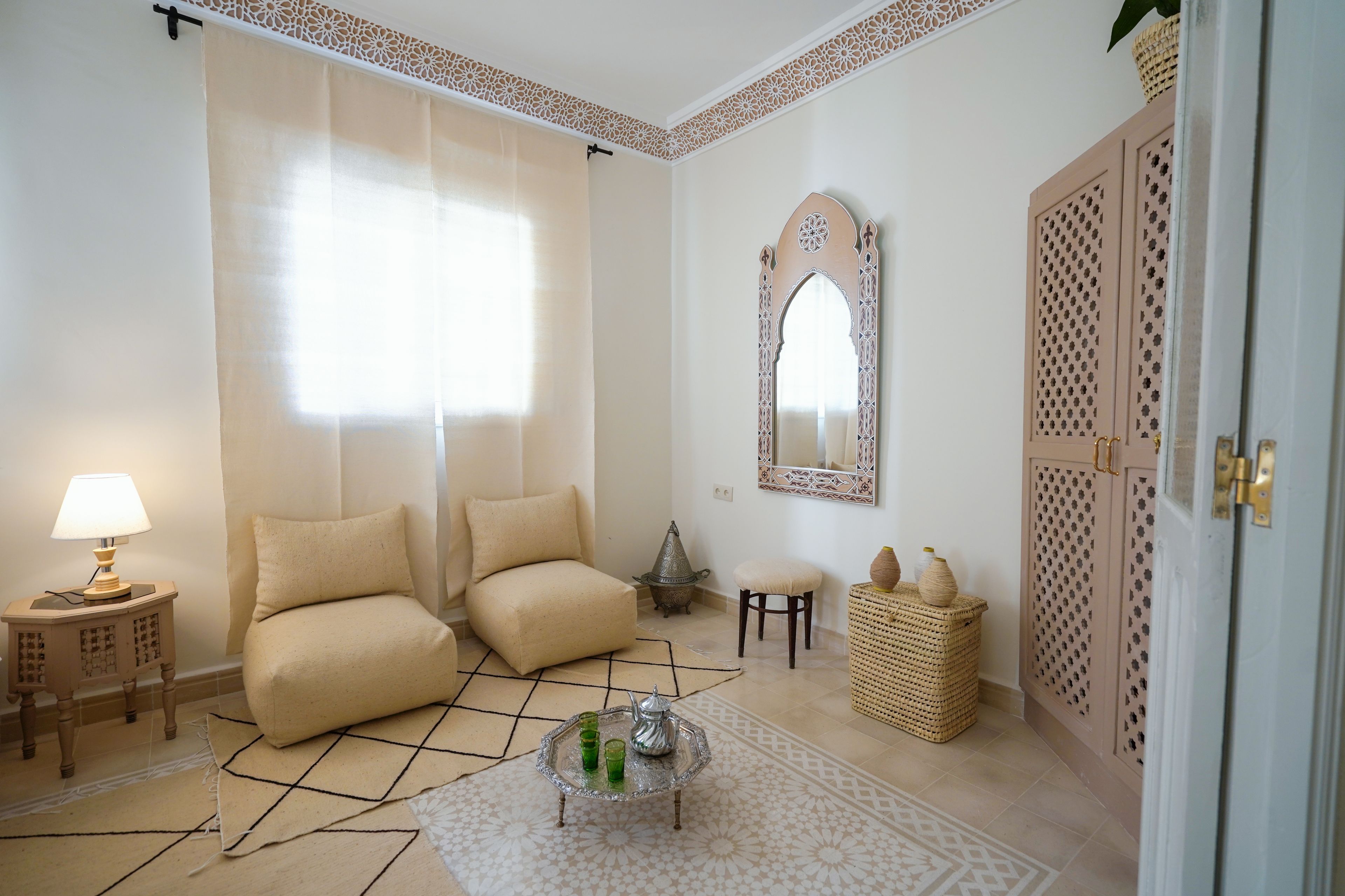 Une pièce comprenant un canapé, une table basse, une lampe, un miroir décoratif et une porte ornée d’un motif.