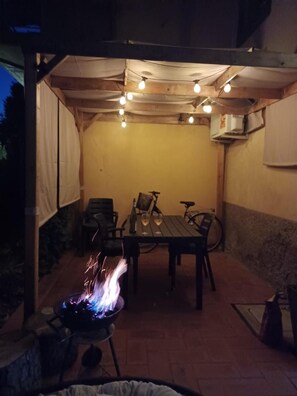 En udendørs terrasse med et bord, stole og grill.