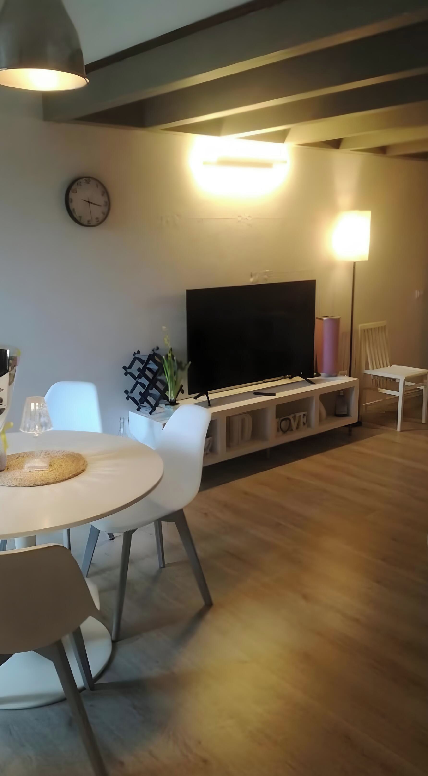 Un salon moderne comprenant un coin repas, un téléviseur à écran plat et une horloge murale.