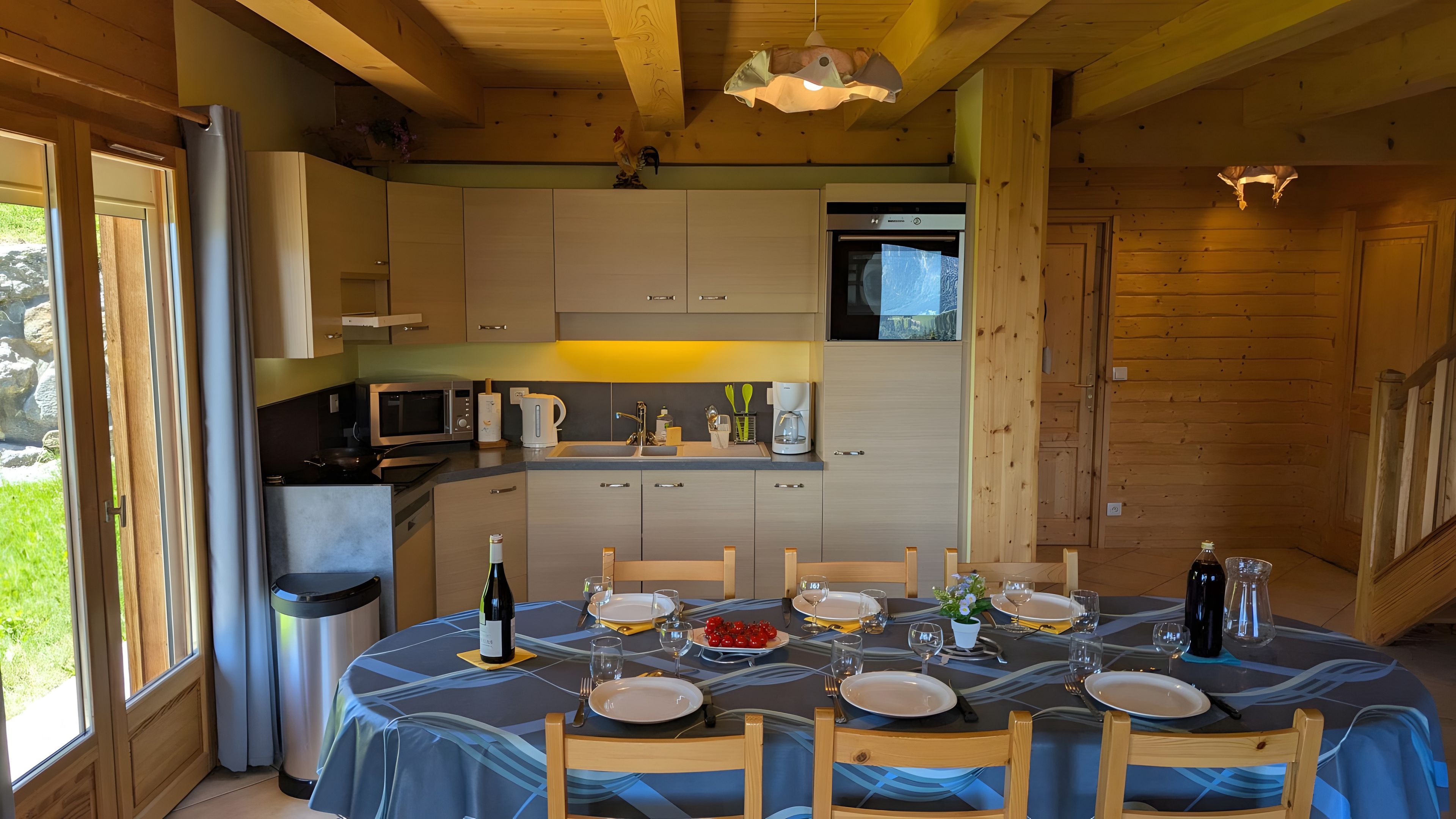 Une cuisine moderne dotée d’appareils électroménagers intégrés, un coin repas aménagé pour quatre personnes avec une table dressée, et des murs en bois.