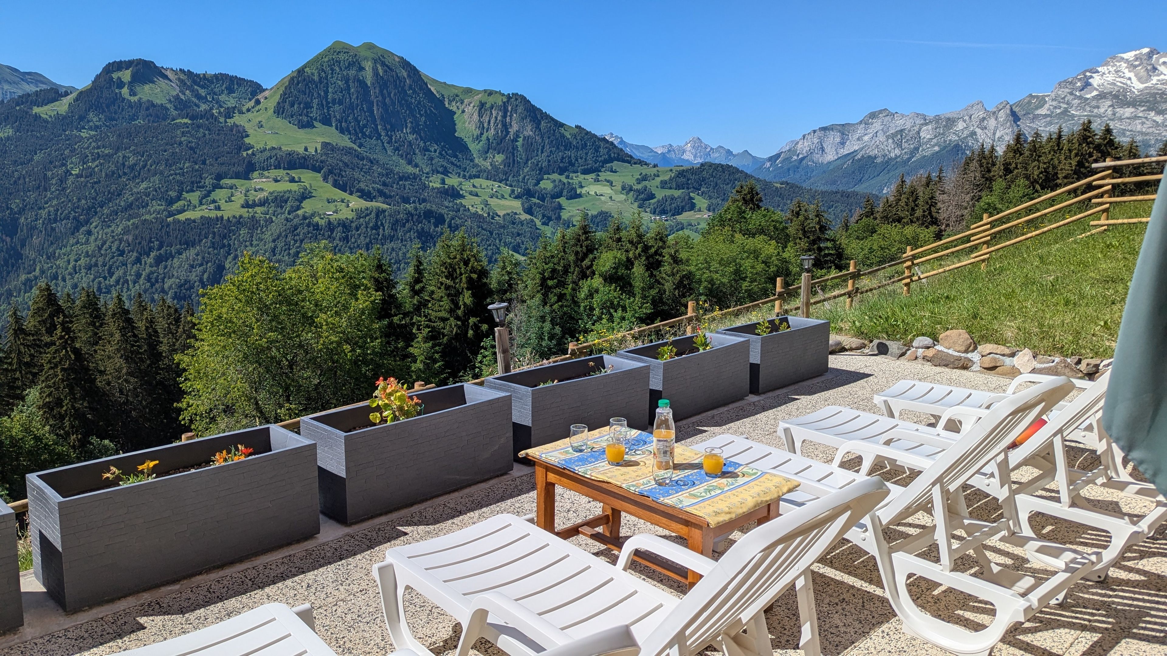 A terrace with outdoor seating, a table with drinks, and a mountain view.