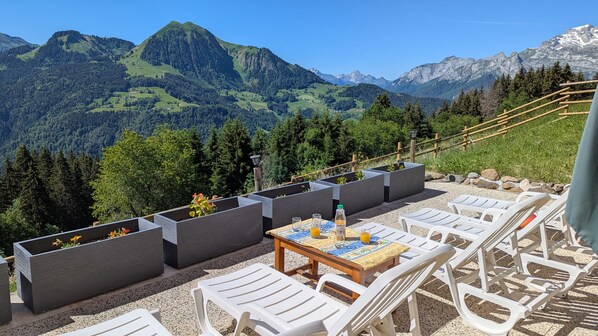 A terrace with outdoor seating, a table with drinks, and a mountain view.