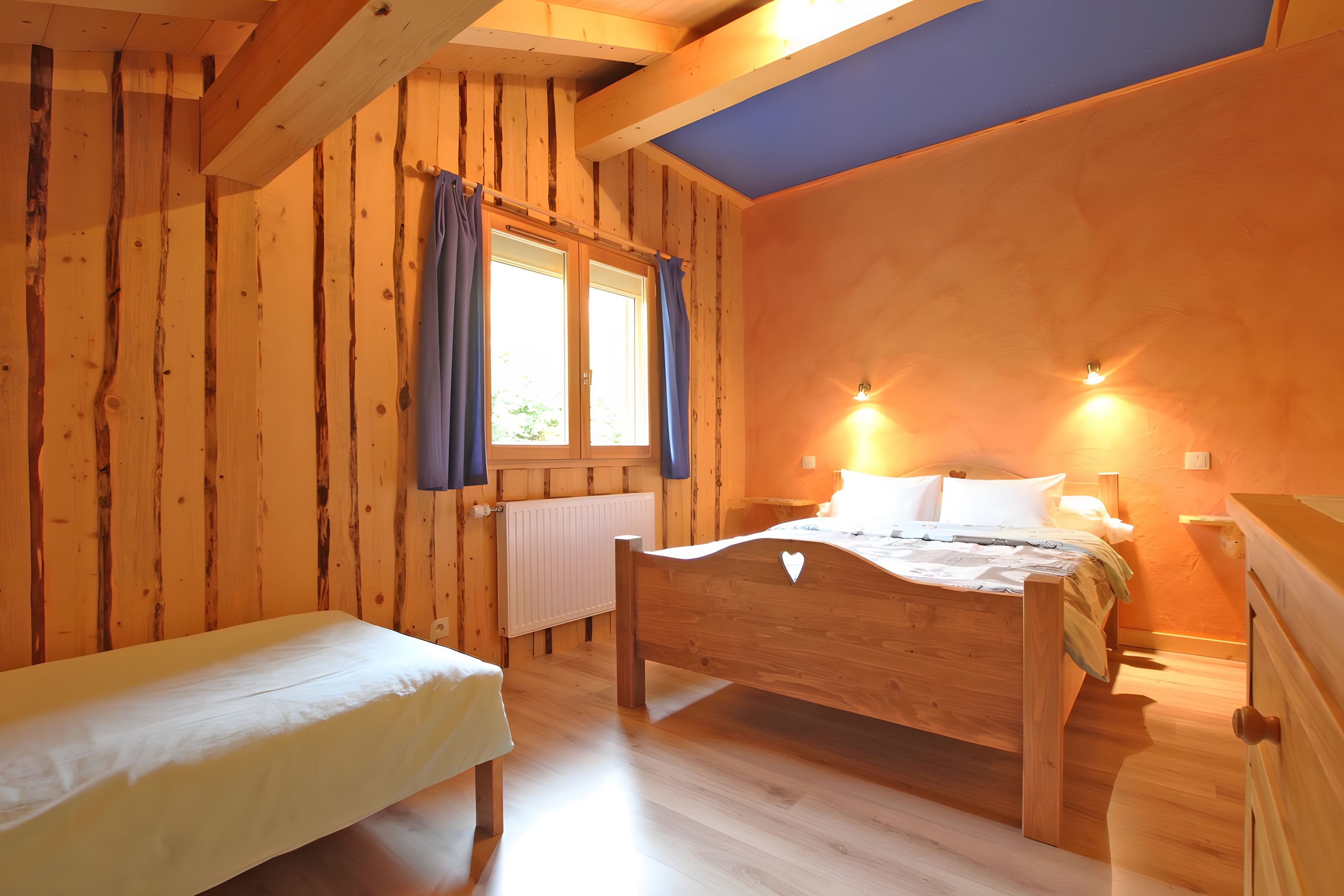 A wooden room with a bed, a bench, and a window with curtains.