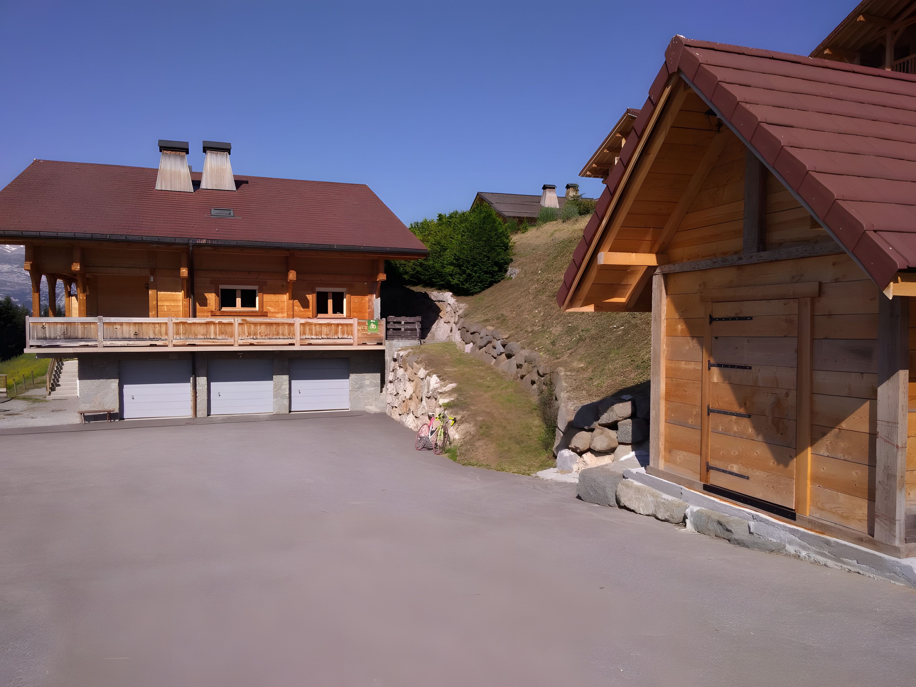 A wooden cabin with a balcony, a garage, and a stone retaining wall.