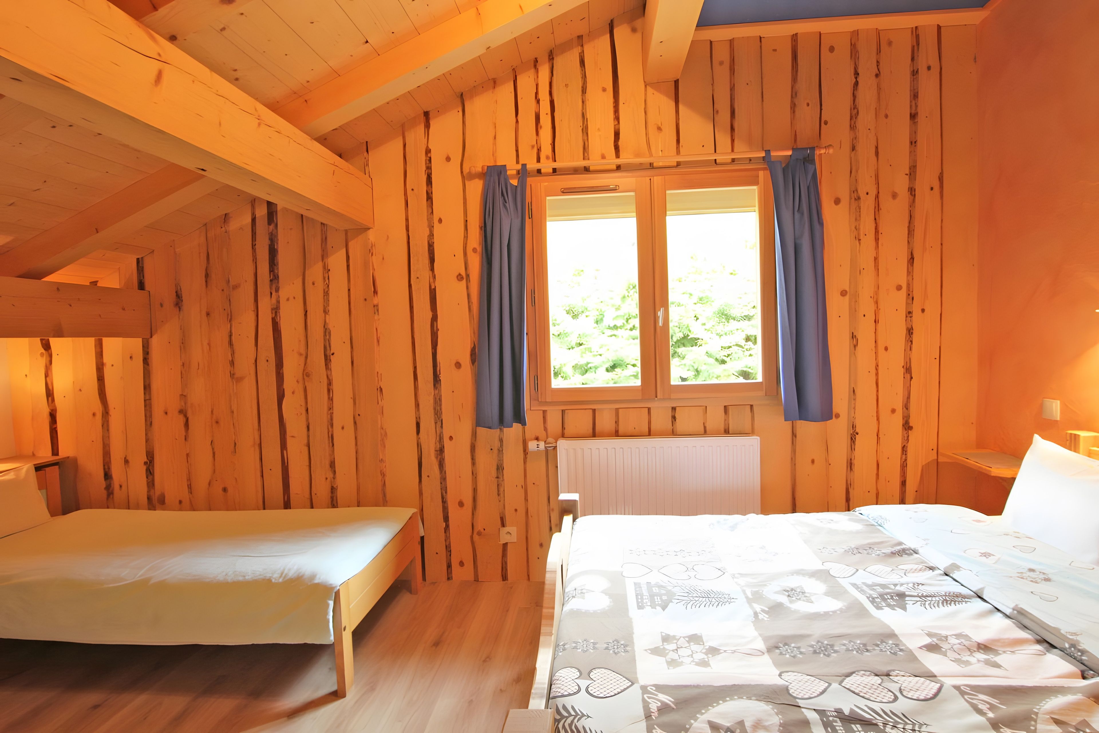 Ein Holzhütten-Zimmer mit einem Bett, einem kleinen Tisch und einem Fenster mit Vorhängen.