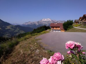 Ein Berggasthof mit gepflasterter Auffahrt, umgeben von Grün und mit Blick auf die Berge.