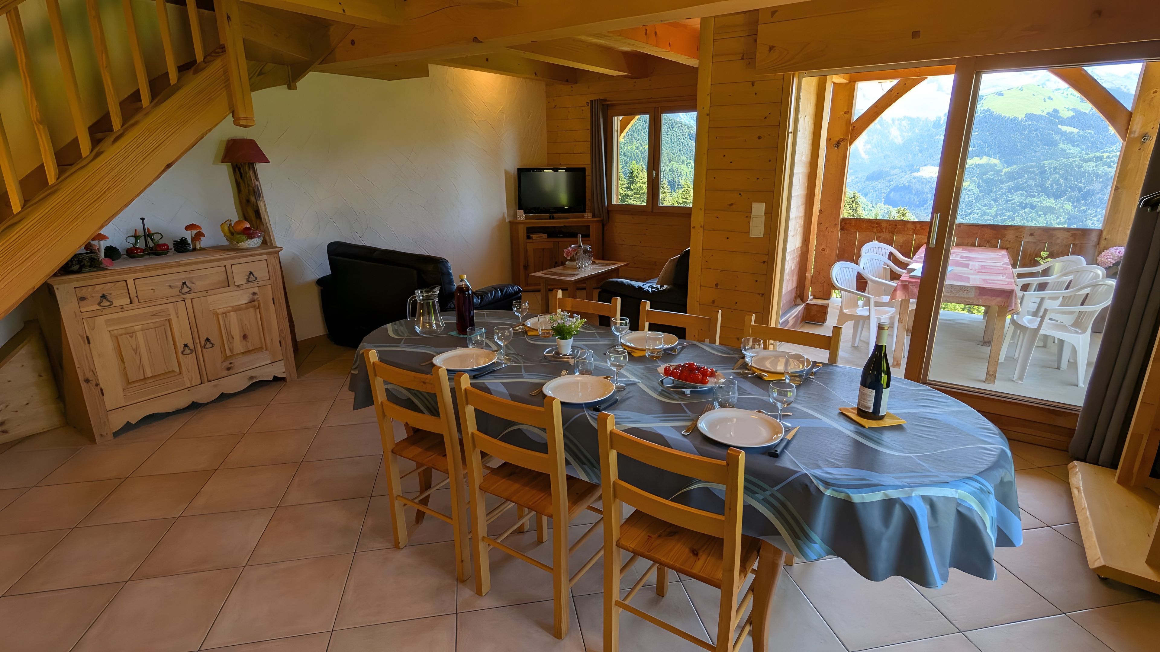 Ein Essbereich mit einem Tisch für vier Personen, Holzstühlen, einem Fernseher und Bergblick durch große Fenster.