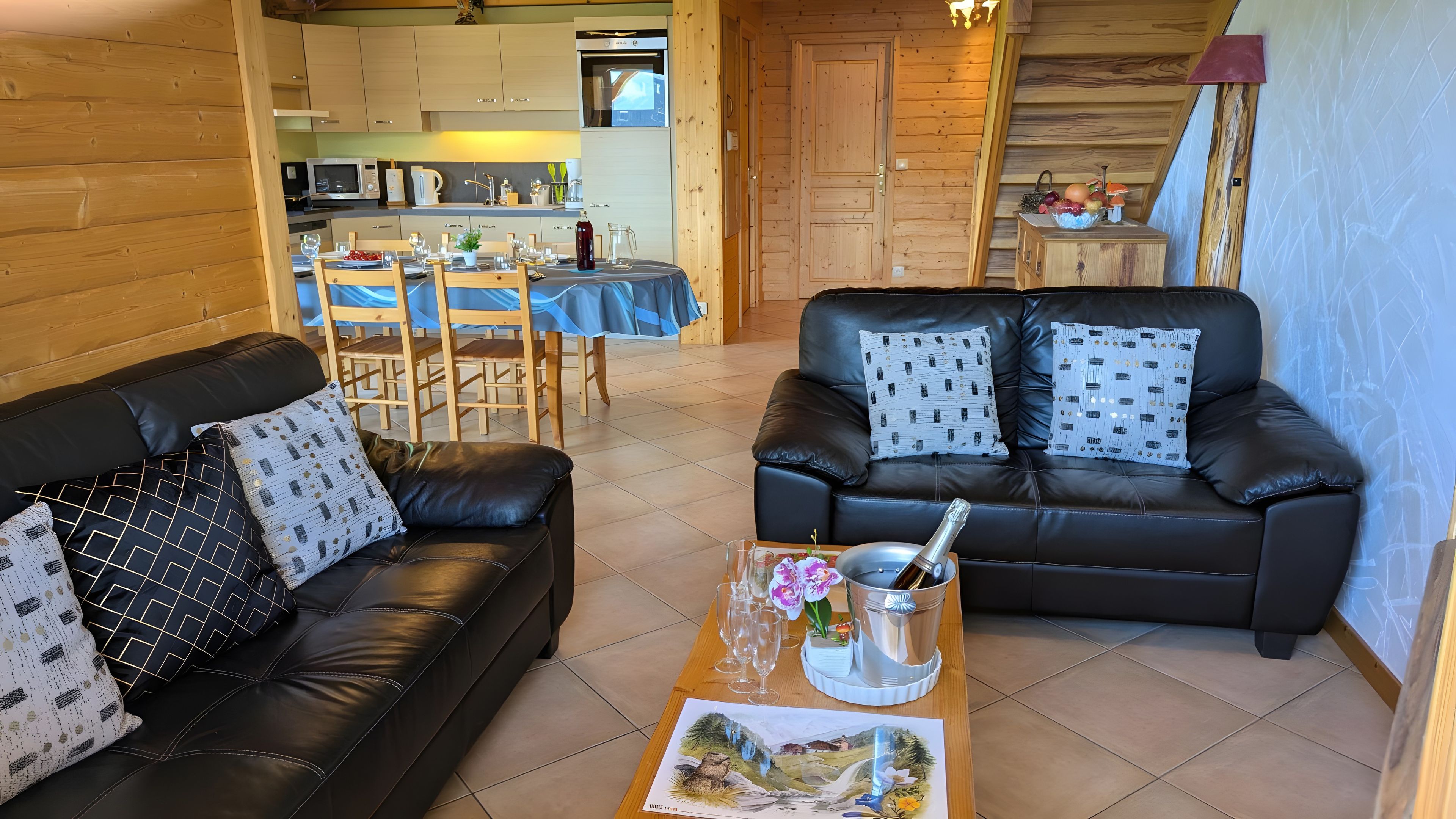 Ein gemütliches Wohnzimmer mit einer schwarzen Ledersofa, einem Esstisch mit Stühlen und einer Küche im Hintergrund.