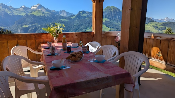 Una terrassa de fusta amb una taula preparada per dinar, caires de plàstic blancs i vista a les muntanyes.