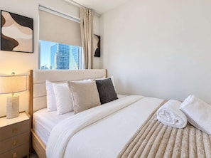 Habitación de hotel con una cama, una mesita de noche, una lámpara y una ventana con vista a la ciudad.