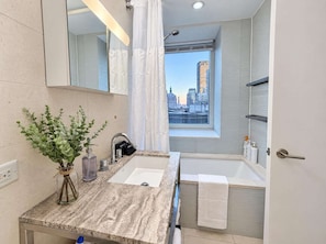 Un baño moderno con encimera de mármol, un espejo grande, un ventanal con vistas a la ciudad y una bañera.