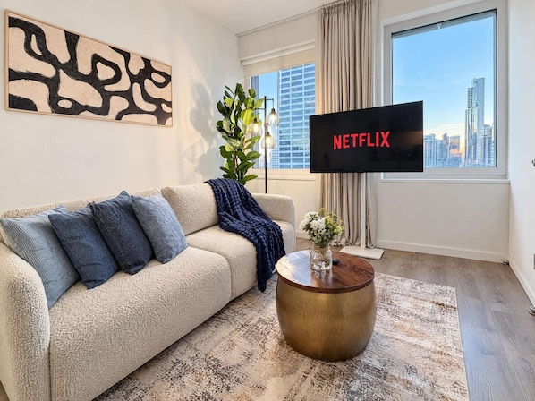 Uma sala de estar com sofá, mesa de centro, planta e uma TV exibindo 'NETFLIX'.
