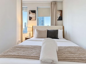 Quarto de hotel com cama, janela com cortinas, luminária e obra de arte na parede.