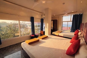 A hotel room with two beds, a large window with a view, a ceiling fan, and a small table with a red stool. - Hotel O Pearl Marine (Port-Blair)