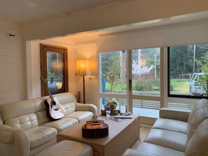A living room with a beige sofa, a coffee table, a guitar, and a lamp. - Forest Cottage Bed-n-breakfast (Reefton)