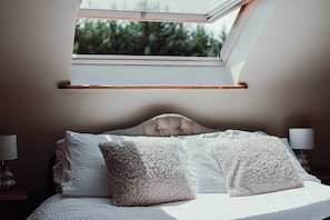 Un dormitorio con tragaluz, una cama con sábanas blancas y dos almohadas con textura.