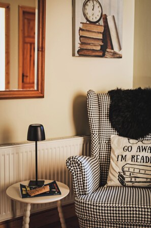 Un coin lecture confortable avec un fauteuil à motif pied-de-poule, une petite table d’appoint avec une lampe et une horloge murale.