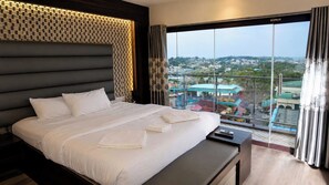A hotel room with a large bed, a view of a cityscape through floor-to-ceiling windows, and a balcony with a railing. - Hotel O Seagull (Port-Blair)